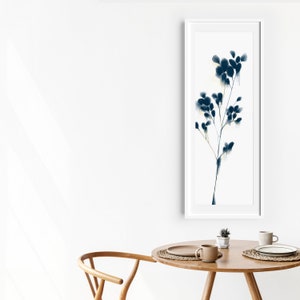 Peut inclure: Une impression encadr&eacute;e blanche avec une peinture &agrave; l'aquarelle bleue d'une branche stylis&eacute;e avec des feuilles. L'impression est accroch&eacute;e &agrave; un mur blanc au-dessus d'une table en bois avec deux tasses et une plante.