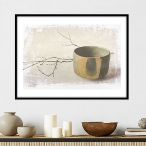 May include: A framed print featuring a ceramic bowl with a unique design. The bowl is primarily olive green with vertical stripes of tan and light blue. A delicate branch extends across the background, adding a natural element to the composition.