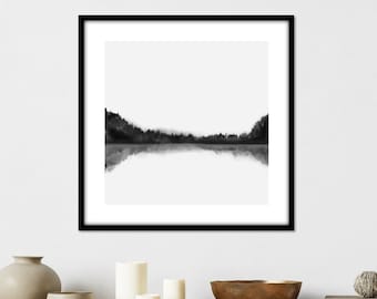 May include: Black and white minimalist art print of a forest reflected in a still lake. The print is framed in a black frame and hangs on a white wall.