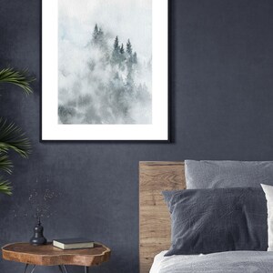 Op de afbeelding: Een ingelijst aquarel schilderij van een mistige bossen sc&egrave;ne met hoge, donkergroene bomen. Het schilderij is in een zwarte lijst en hangt aan een donkergrijze muur.