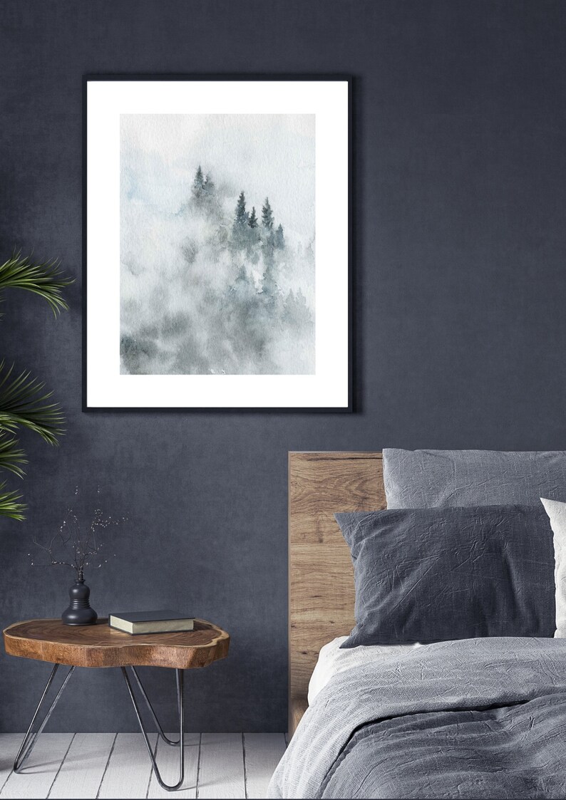 Op de afbeelding: Een ingelijst aquarel schilderij van een mistige bossen sc&egrave;ne met hoge, donkergroene bomen. Het schilderij is in een zwarte lijst en hangt aan een donkergrijze muur.