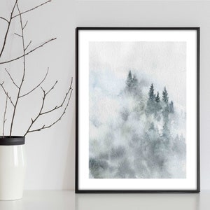 Op de afbeelding: Een aquarel schilderij van een mistige bossen sc&egrave;ne met donkergroene bomen gesilhouetteerd tegen een lichtblauwe en grijze achtergrond.