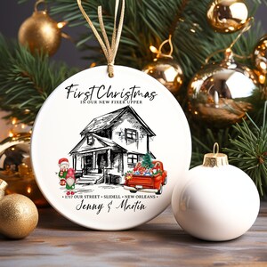 May include: White ceramic Christmas bauble featuring a black and white illustration of a house and a red truck. The text "First Christmas in our new fixer upper" is written above the house. The text "1717 Our Street, Slidell, New Orleans" is written below the house. The text "Jenny & Martin" is written below the address.