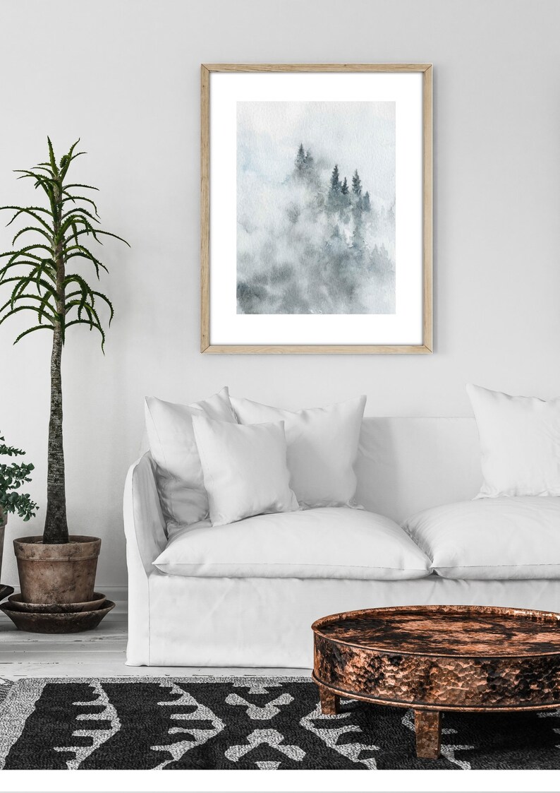 Op de afbeelding: Een ingelijst aquarel schilderij van een mistige bossc&egrave;ne met hoge, donkergroene bomen. Het schilderij is in een licht houten lijst en hangt aan een witte muur.