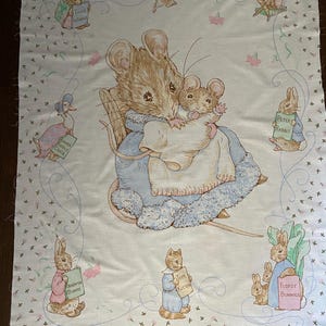 May include: A vintage fabric panel featuring illustrations of Beatrix Potter characters. The central image shows a mother mouse and child. Other characters include Peter Rabbit, Tom Kitten, and Flopsy Bunnies, each holding a sign. The fabric has a floral pattern.