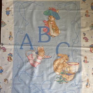 May include: A light blue and cream-colored fabric featuring illustrations of rabbits and mice in a storybook style. The fabric has the letters "ABC" in a light blue color, with a decorative border and small illustrations.