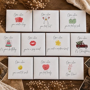May include: A set of eleven white envelopes with black text and colourful illustrations. Each envelope features the phrase Open when followed by specific prompts like you need a hug, you feel lost, you're feeling sick, it's your birthday, you're a sexy mood, you need a confidence boost, it's Christmas, you want to smile, you feel lonely, or Open Now.