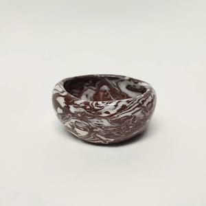 May include: A small, round bowl with a brown and white marbled design. The bowl is made of ceramic and has a smooth, glossy finish.