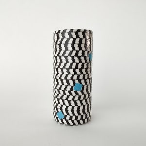 May include: A black and white ceramic vase with a wavy pattern and three blue squares. The vase is cylindrical and has a smooth, glossy finish.