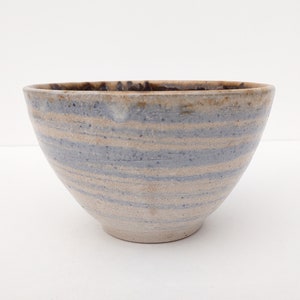 May include: A small, white ceramic bowl with blue and brown stripes. The bowl is hand-thrown and has a rustic, handmade look.