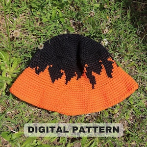 May include: A handmade crochet bucket hat in black and orange, with a unique flame-like design where the colors meet. The hat is displayed on a bed of green grass. The text "DIGITAL PATTERN" is displayed at the bottom of the image.