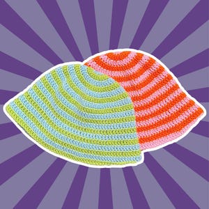 May include: Two crochet bucket hats featuring horizontal stripes. One hat displays alternating light blue and lime green stripes, while the second hat behind it showcases alternating bright orange and soft pink stripes in a circular pattern.