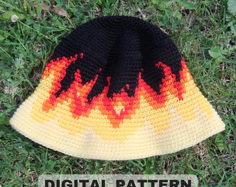 May include: A crochet bucket hat with a black crown and a yellow, orange, and red flame design. The hat is on a bed of green grass. "DIGITAL PATTERN" is written in white text on a black background at the bottom of the image.