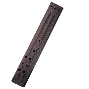 May include: A dark brown, textured, rectangular object with circular and rectangular cutouts. It features a ridged design and is angled diagonally against a white background. The surface has a speckled appearance.