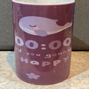 Op de afbeelding: Paarse keramische mok met een cartoon walvis illustratie. De mok heeft de witte tekst "00:00 and you gonna Happy". Een kleine bloemengrafiek staat onderaan. De mok is cilindrisch en heeft een witte binnenkant.