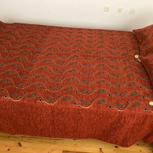 May include: A red and gold patterned bedspread with a wave design and a matching pillow. The bedspread is made of a soft, textured fabric.
