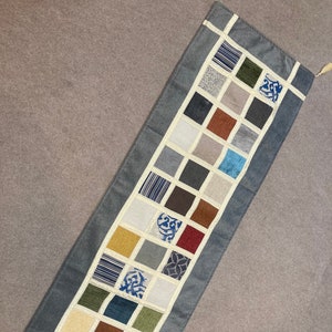 May include: A blue table runner with a patchwork design featuring squares of various colors and patterns, including brown, beige, green, blue, and red.