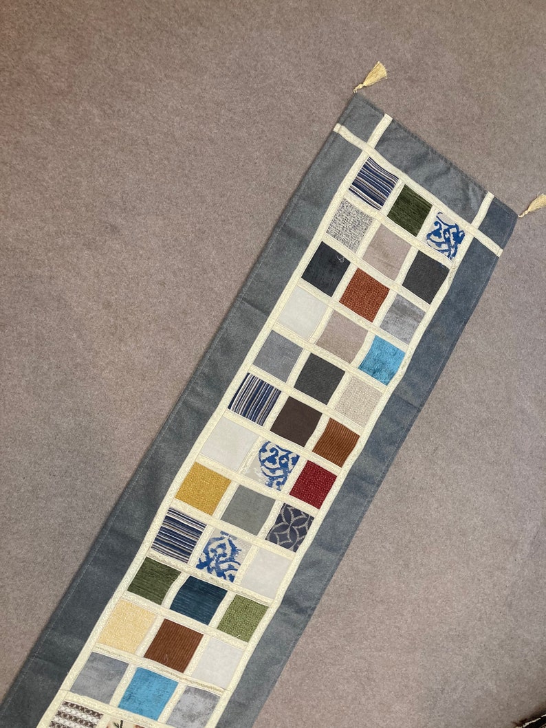 May include: A blue table runner with a patchwork design featuring squares of various colors and patterns, including brown, beige, green, blue, and red.