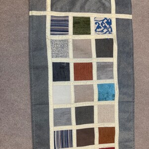 May include: A gray rectangular runner rug with a patchwork design. The rug is made of different fabrics in various shades of gray, brown, blue, and white. The rug has a fringe on each end.