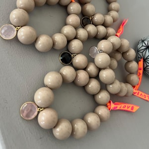 Könnte beinhalten: Beige Perlenarmbänder mit goldenen Akzenten und Edelsteinanhängern. Jedes Armband hat große, runde Perlen und ist mit einem Anhänger und einem neonorangenen Band mit dem Wort "LOVE" verziert. Ein modisches Accessoire.
