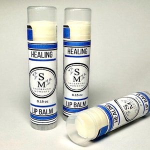Può includere: Tre tubetti di balsamo per le labbra con balsamo bianco all'interno. I tubetti hanno un'etichetta bianca con strisce blu e le parole "HEALING" e "LIP BALM". L'etichetta presenta anche il testo "SM Sagebrush Moments" e "0,15 oz".