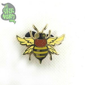 May include: A gold-colored bee pin with yellow and black stripes, red and black eyes, and yellow wings.