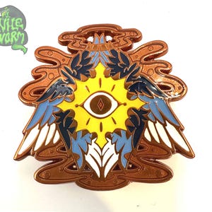 May include: An ornate enamel pin with a central eye design set within a yellow sunburst, framed by blue and white wings. The pin has a copper-coloured border and the text "The Wild Worm" in green.