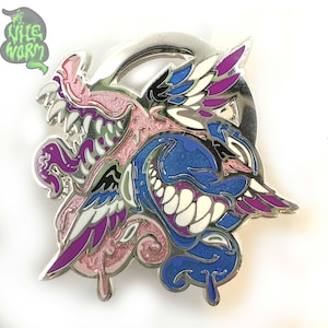 Puede incluir: Un pin de esmalte plateado con un diseño colorido de dos caras monstruosas sonrientes. El pin incorpora colores rosa, azul, morado y blanco, con el texto "Wile Worm" en una burbuja verde.