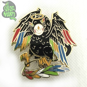 May include: A black enamel pin with a gold outline depicting a bird with rainbow wings and a halo. The bird is holding a feather in its talons.