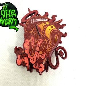 Puede incluir: Pin de dibujos animados detallado que representa una criatura con órganos internos, una cola y un halo. El pin es principalmente de color rojo, marrón y naranja con detalles de purpurina. El texto "Wile Worm" es verde con un contorno negro.