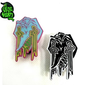 May include: Two enamel pins with a dripping, melting, abstract design. The pins are black and white and blue and green. The pins are shaped like a head with a dripping, melting, abstract design. The pins are both about 2 inches tall.