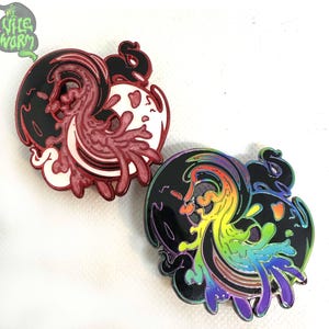 May include: Two enamel pins with a yin yang design. One pin is red and white, the other is rainbow and black.