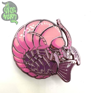 Puede incluir: Un pin de esmalte rosa y morado que representa una criatura insectoide estilizada. El pin tiene un acabado brillante con un diseño detallado, que incluye partes del cuerpo segmentadas y una aleta caudal. El pin es un artículo de colección.