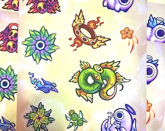 May include: A sheet of colorful stickers featuring whimsical characters and designs. The stickers include a green snake with wings, a purple creature with a halo, a flower with a star, and a ring with flames.