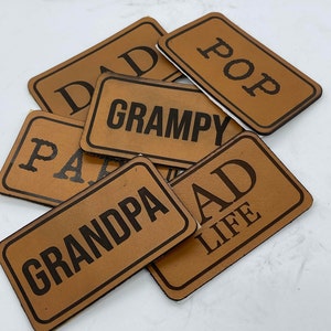 May include: Six brown leather patches with black text. The patches read "Dad", "Pop", "Grampy", "Pa", "Grandpa", and "Dad Life".