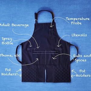May include: Black apron with multiple pockets and quilted pot holders. The pockets are labeled with the text "Adult Beverage", "Spray Bottle", "Phone, etc", "Temperature Probe", "Utensils", "Rubs and Spices".