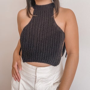 May include: A black halter top with a high neckline and open sides. The top is made of a knitted material and has tie closures at the sides. The garment is paired with white pants.