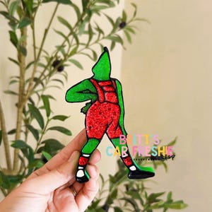 May include: A green and red glittery car air freshener shaped like a character in overalls, with black outlines and black shoes. The text "BRITT'S CAR FRESHIES Shop" is printed in colorful letters on the right side of the figure.