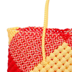 Könnte beinhalten: Eine gelbe und rote karierte Plastiktüte mit einem einzigen gelben Henkel.
