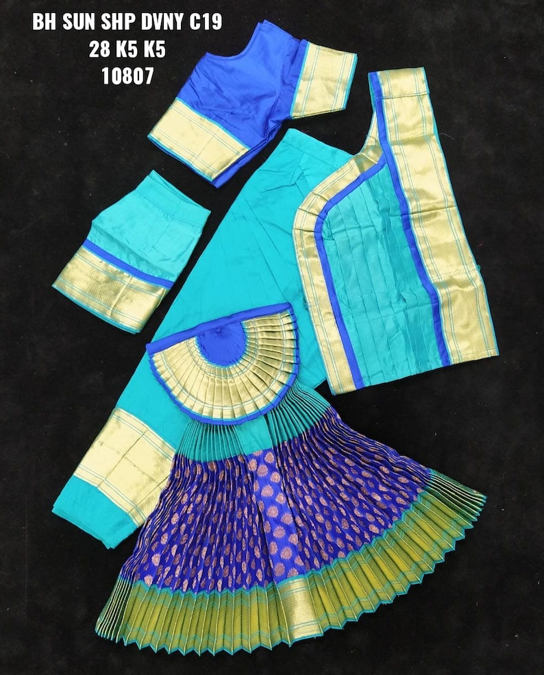 Puede incluir: Un traje de danza indio azul y verde con ribetes dorados. El traje incluye una falda, una blusa y una chalina. La falda est&aacute; plisada y tiene un patr&oacute;n azul y dorado. La blusa es azul y tiene ribetes dorados. La chalina es verde y tiene ribetes dorados. El traje est&aacute; etiquetado como "BH SUN SHP DVNY C19 28 K5 K5 10807".