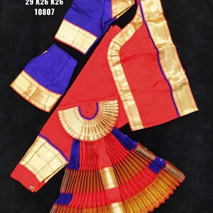 Puede incluir: Traje de danza indio rojo y azul con ribetes dorados. El traje incluye una falda, una blusa y una pieza decorativa para la cintura. El texto en la imagen dice "BH SUN SHP DVNY C19 29 K26 K26 10807".