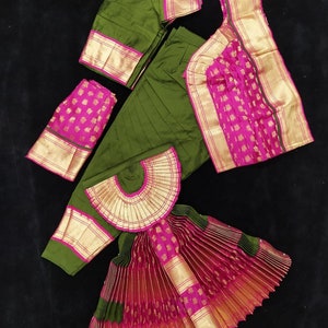 Puede incluir: Un traje de danza indio verde y rosa con una falda plisada, una blusa y un tocado a juego. La falda est&aacute; hecha de una tela verde y rosa con ribetes dorados. La blusa es verde con ribetes dorados y un borde rosa. El tocado es una pieza de tela en forma de abanico con ribetes dorados.