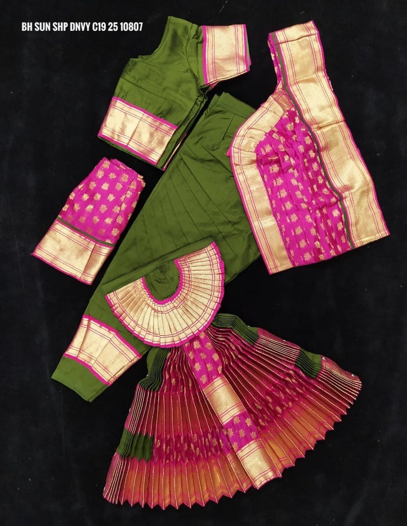 Puede incluir: Un traje de danza indio verde y rosa con una falda plisada, una blusa y un tocado a juego. La falda est&aacute; hecha de una tela verde y rosa con ribetes dorados. La blusa es verde con ribetes dorados y un borde rosa. El tocado es una pieza de tela en forma de abanico con ribetes dorados.