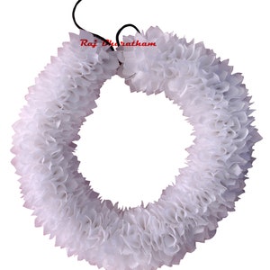 May include: White artificial flower garland, made of fabric, in the shape of a circle. The garland is tied together with a black string.