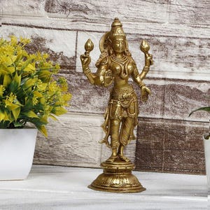 May include: A gold-colored metal statue of a Hindu goddess with four arms holding lotus flowers. The statue is standing on a round base with intricate details.
