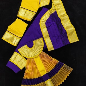 Puede incluir: Un traje de danza indio amarillo y morado con una falda plisada, una blusa y un abanico decorativo. La falda est&aacute; hecha de tela amarilla y morada con ribetes dorados. La blusa es amarilla con ribetes dorados. El abanico est&aacute; hecho de tela dorada con un dise&ntilde;o amarillo y morado. El traje est&aacute; etiquetado como "BH SUN SHP DNVY 25.5 K42-K32 132".