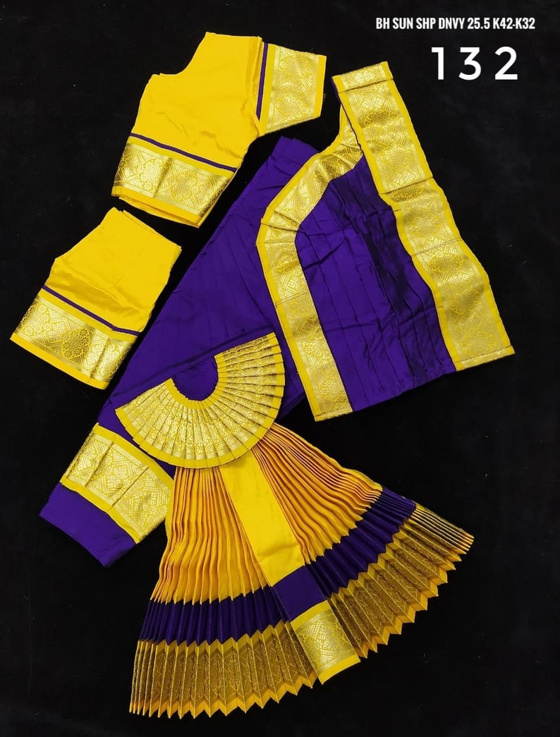 Puede incluir: Un traje de danza indio amarillo y morado con una falda plisada, una blusa y un abanico decorativo. La falda est&aacute; hecha de tela amarilla y morada con ribetes dorados. La blusa es amarilla con ribetes dorados. El abanico est&aacute; hecho de tela dorada con un dise&ntilde;o amarillo y morado. El traje est&aacute; etiquetado como "BH SUN SHP DNVY 25.5 K42-K32 132".