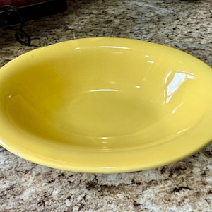 May include: A large, yellow ceramic bowl with a smooth, glossy finish. The bowl is empty and has a slightly oval shape.