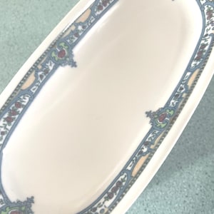 May include: An oval-shaped, white ceramic dish with a blue, green, and yellow floral border.