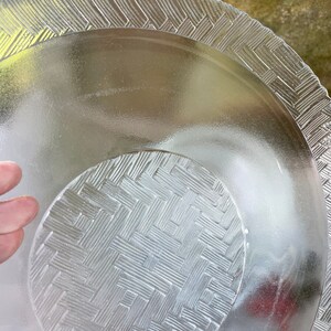 May include: Clear glass serving dishes with textured basketweave and geometric patterns. The set includes a large plate and a smaller, nested dish. The edges of the plates have a decorative, raised design.